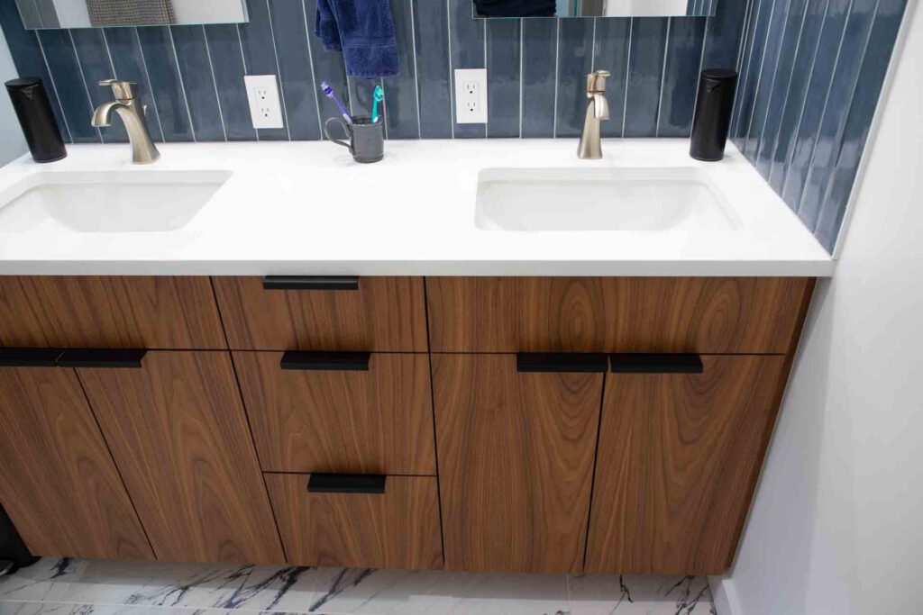 Bathroom vanity with dual sinks and blue tile backsplash Bathroom vanity with double sinks, brushed metal faucets, blue tile backsplash, and wooden cabinets.