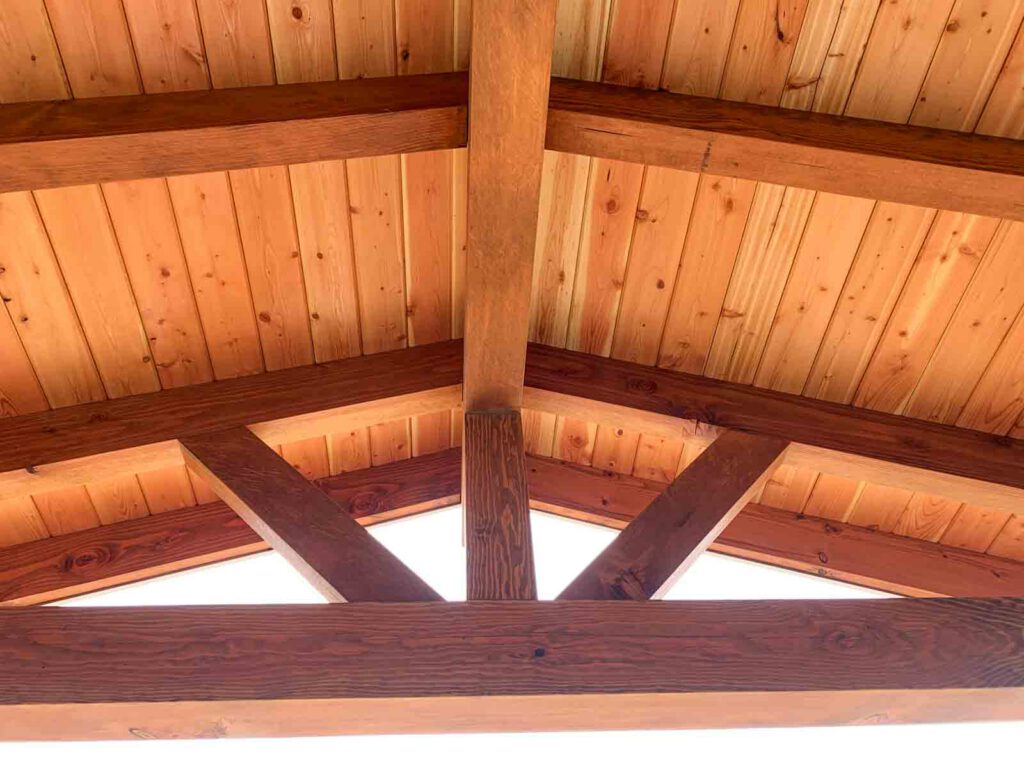 Wooden ceiling with light planks and dark exposed beams in triangular roof pattern.