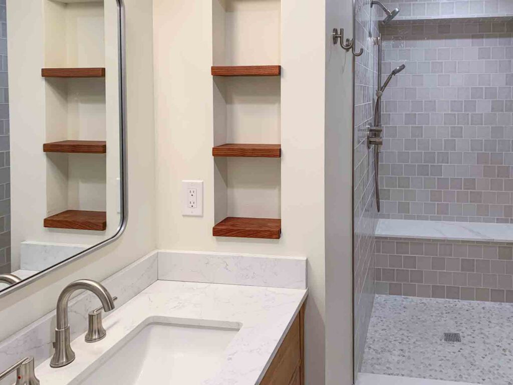 Modern bathroom with marble countertop and walk-in shower Bathroom with white marble countertop, undermount sink, wooden shelves, and tiled walk-in shower.