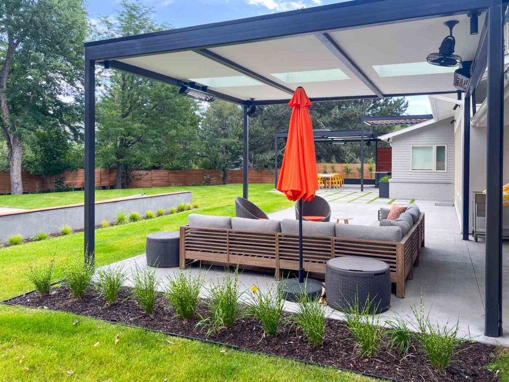 Modern outdoor patio with pergola and seating Modern outdoor patio with wooden sectional sofa, orange umbrella, and green lawn.