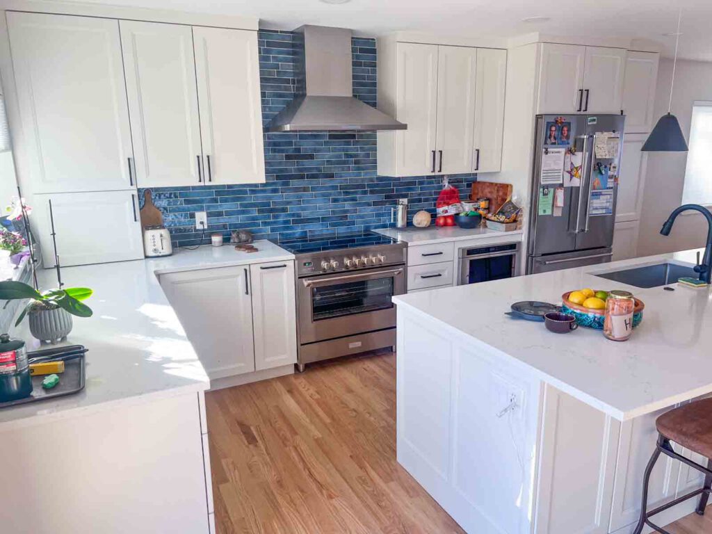 Modern kitchen with white cabinets, blue tile backsplash, stainless appliances, and island with sink.