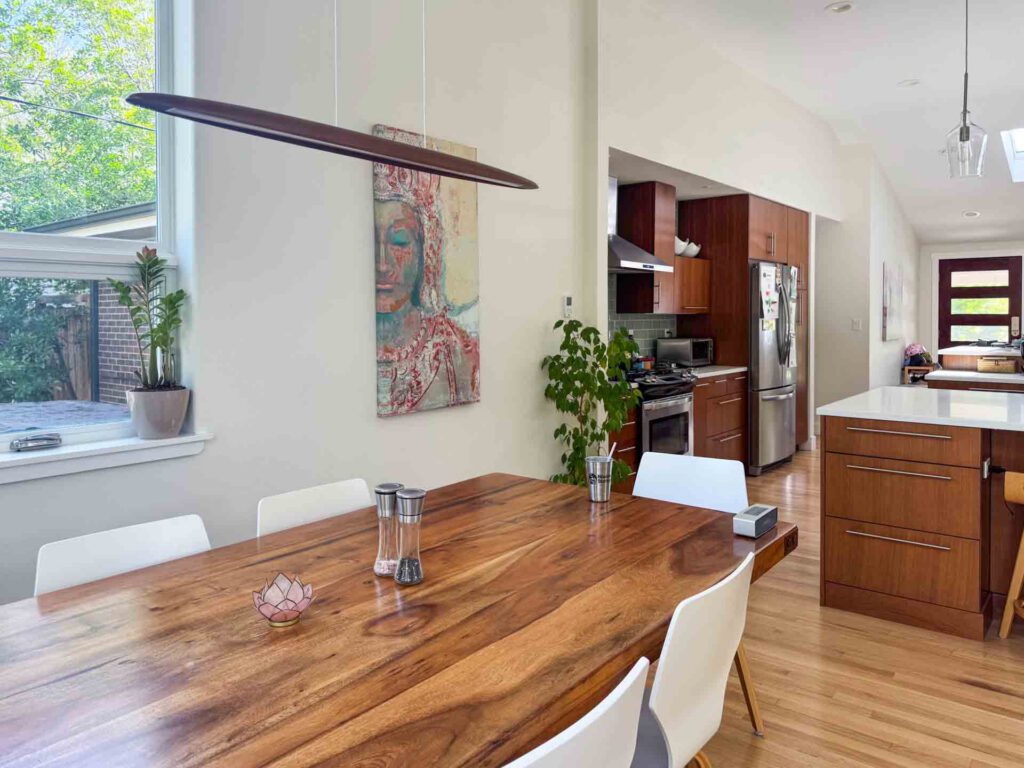 Modern dining area with open kitchen and wooden accents Dining area with wooden table, white chairs, open kitchen, wooden cabinets, and stainless appliances.