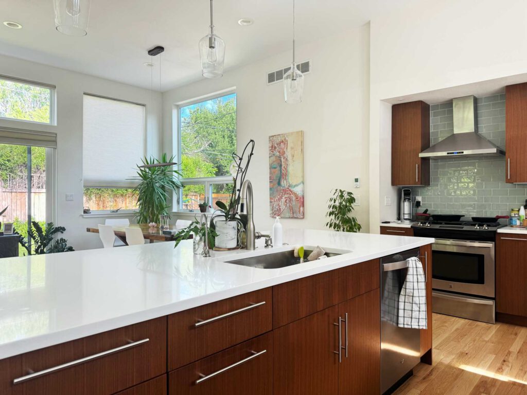 Modern kitchen with white island and stainless steel appliances Modern kitchen with white island, wood cabinets, stainless appliances, green tile backsplash, and dining area.
