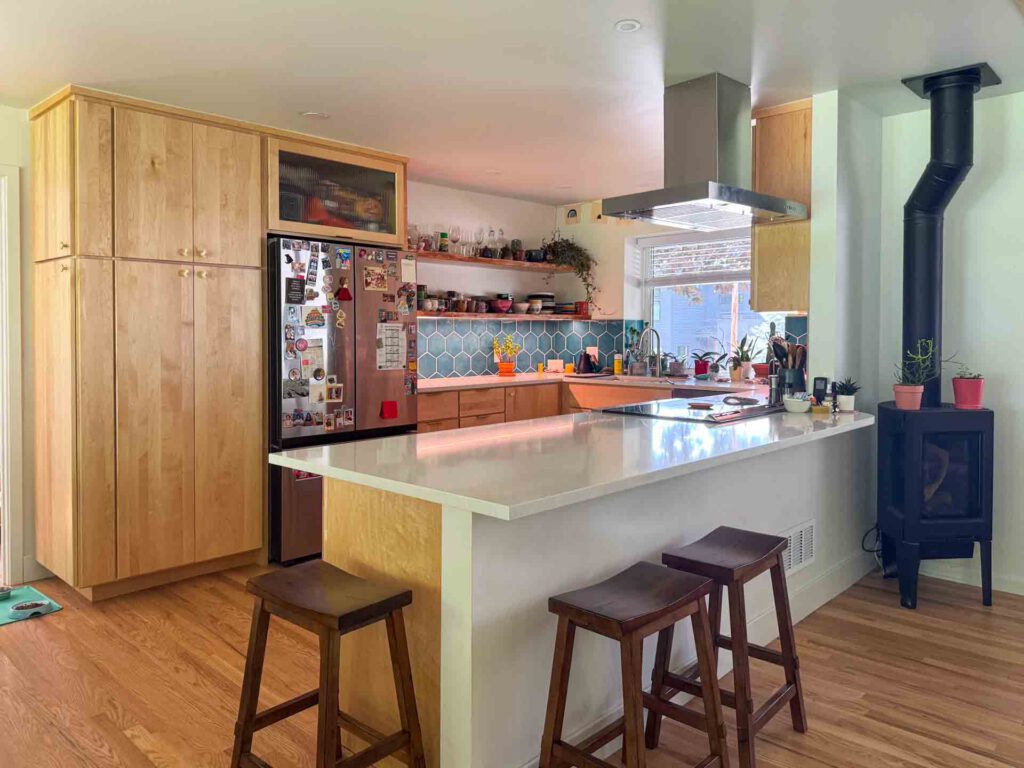 Modern kitchen with blue tile backsplash and wood-burning stove Modern kitchen with wood cabinetry, white island, blue tile backsplash, wood stove, and decorated refrigerator.