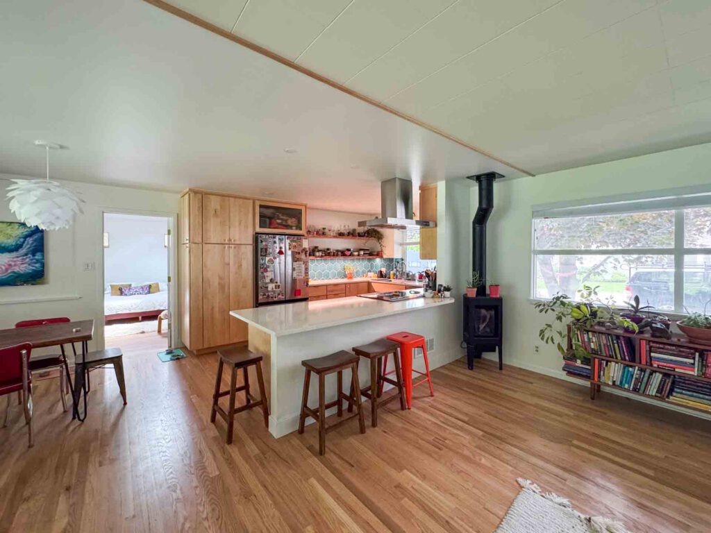 Modern kitchen and dining area with wood accents Open kitchen and dining area with wooden floors, stools, wood-burning stove, and visible bedroom.