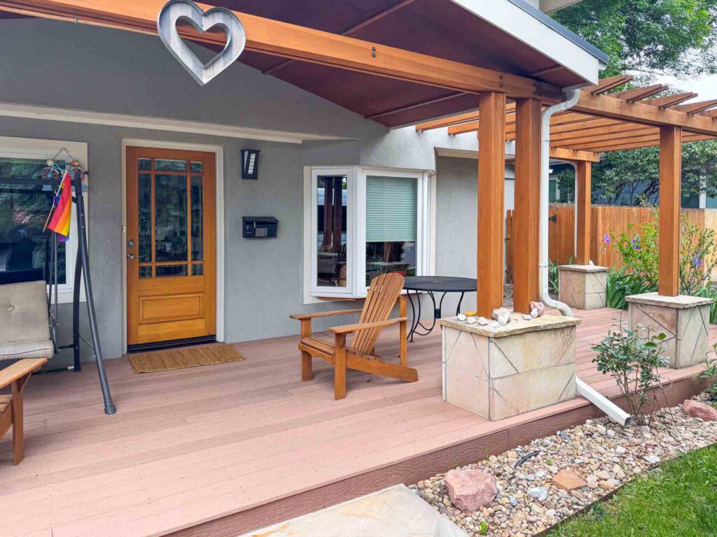 Wooden Porch with Swing and Adirondack Chair Wooden porch with a door, swing, Adirondack chair, black round table, pergola columns, and garden rocks.