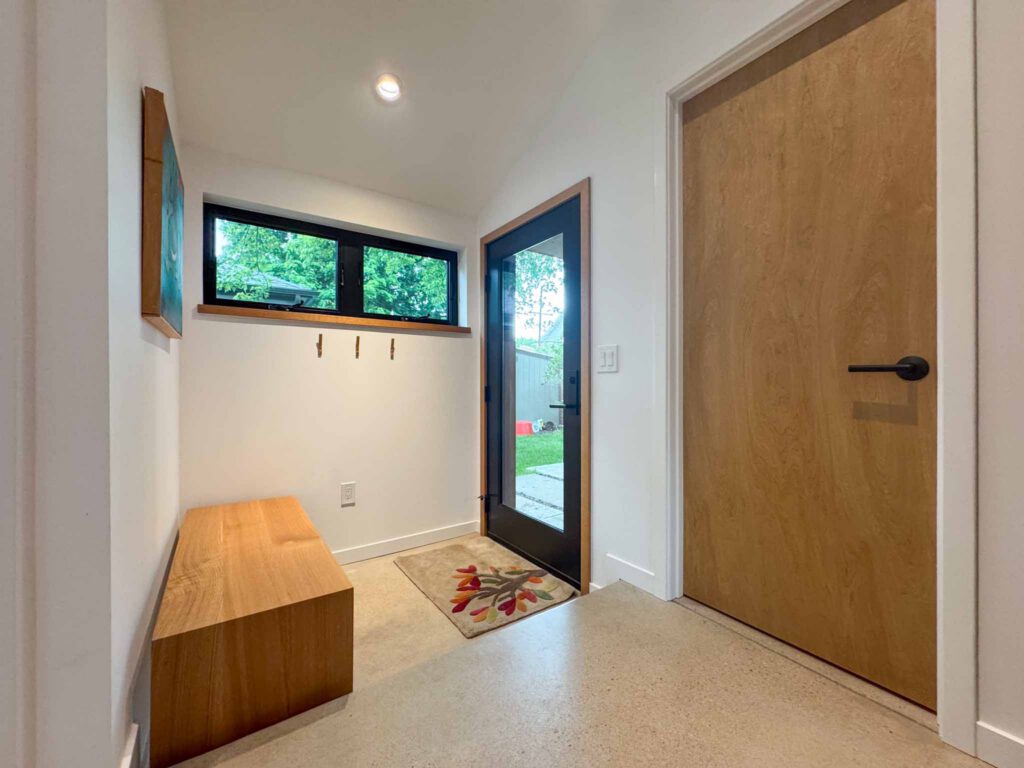 Entryway with glass door, wooden bench, and leaf-patterned rug Entryway with black-framed glass door, wooden bench, three wall hooks, and leaf-patterned rug.