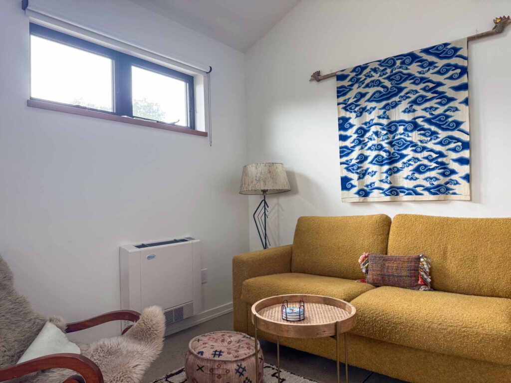 Mustard Yellow Sofa in Cozy Living Room with Cloud Wall Hanging Living room with mustard yellow sofa, wooden side table, patterned pouf, lamp, and blue wall hanging.