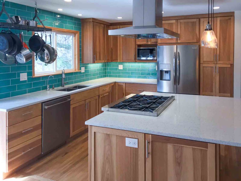 Modern kitchen with wooden cabinets, teal tile backsplash, stainless appliances, and white island with gas cooktop.