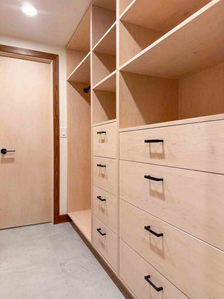 Walk-in closet with light wood drawers, shelves, hanging rod, beige door, and light tile floor.