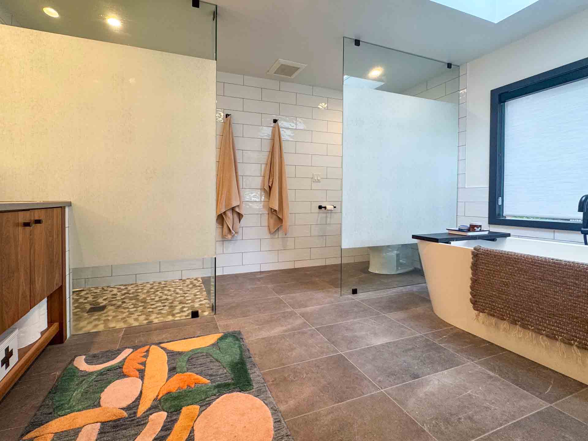 Modern bathroom with freestanding tub, glass shower, textured towels, tiled floors, and colorful rug.